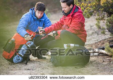 Picture - Male backpackers looking at rope in forest. Fotosearch