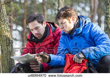 Stock Image - Male backpackers reading map in forest. Fotosearch