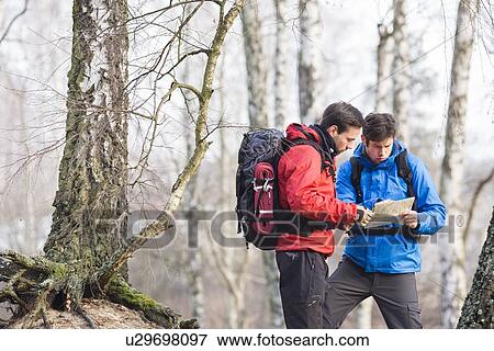 Stock Photo - Male backpackers reading map in forest. Fotosearch