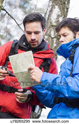 Stock Photography - Male backpackers reading map together in forest. Fotosearch