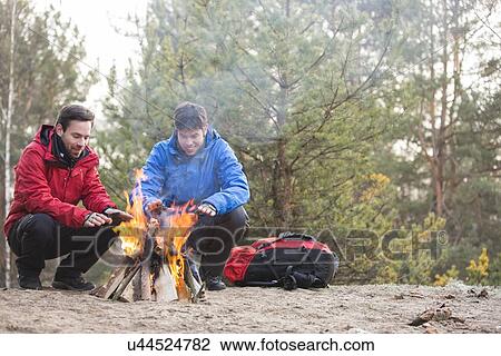 Stock Image - Male backpackers warming hands at campfire in forest. Fotosearch