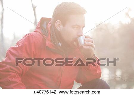 Stock Image - Male hiker drinking coffee in forest. Fotosearch