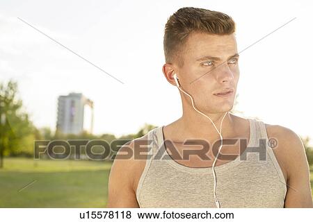 Stock Photo - Male jogger looking away while listening music in park. Fotosearch
