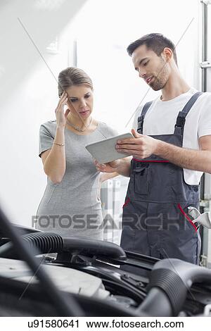 Stock Image - Male maintenance engineer showing digital tablet to worried customer at workshop. Fotosearch