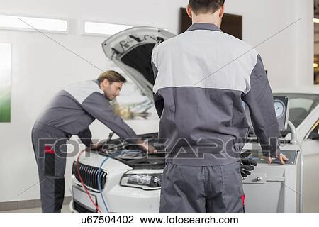 Stock Image - Male maintenance engineers examining car in workshop. Fotosearch