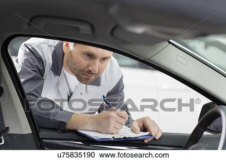 Stock Image - Male mechanic with clipboard checking car's interior in repair shop. Fotosearch