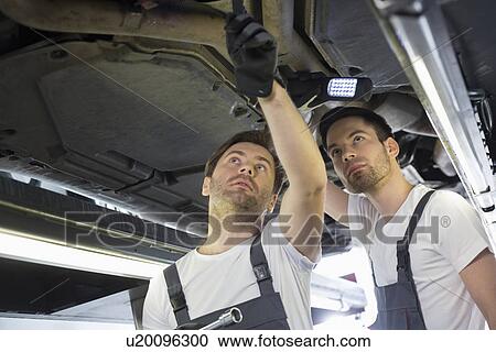 Male mechanics examining car in workshop View Large Photo Image Stock Image - Male mechanics examining car in workshop. Fotosearch