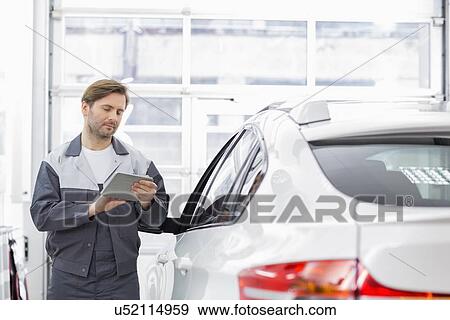 Male repair worker using tablet PC while standing by car in workshop View Large Photo Image Stock Photo - Male repair worker using tablet PC while standing by car in workshop. Fotosearch