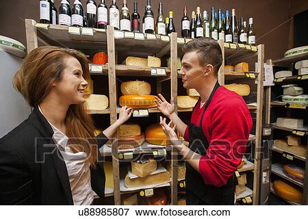 Stock Photo - Male salesperson showing cheese to female customer in store. Fotosearch