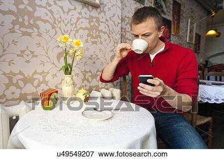 Man having coffee while reading text message on cell phone at cafe View Large Photo Image Stock Photo - Man having coffee while reading text message on cell phone at cafe. Fotosearch