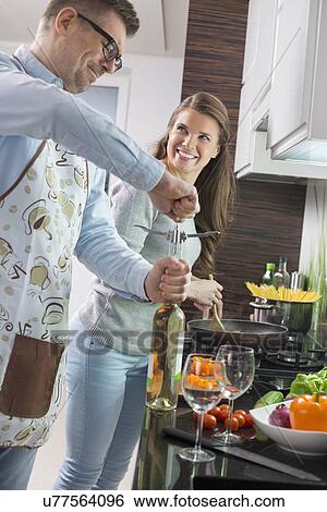 Man opening wine bottle while cooking with woman in kitchen View Large Photo Image Stock Photograph - Man opening wine bottle while cooking with woman in kitchen. Fotosearch