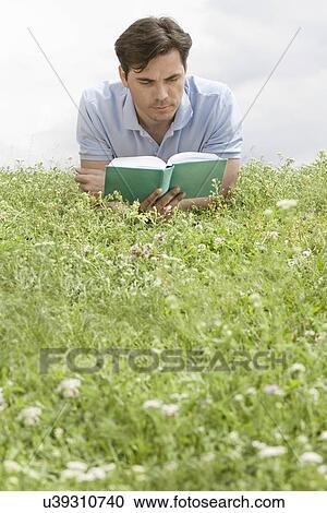 Man reading book while lying on grass against sky View Large Photo Image Stock Image - Man reading book while lying on grass against sky. Fotosearch