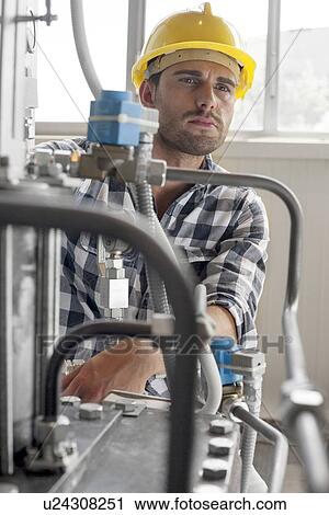 Stock Image - Manual worker looking away while examining machine in industry. Fotosearch
