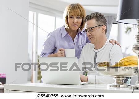 Mature couple using laptop together at table in house View Large Photo Image Stock Photography - Mature couple using laptop together at table in house. Fotosearch