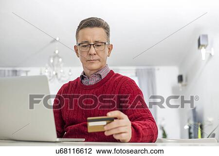 Mature man using credit card and laptop to shop online at home View Large Photo Image Stock Image - Mature man using credit card and laptop to shop online at home. Fotosearch