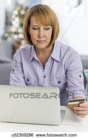Stock Photograph - Mature woman shopping online at home during Christmas. Fotosearch