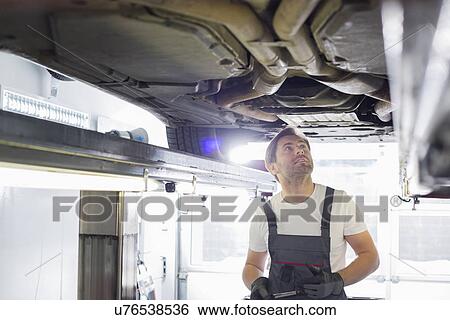 Stock Photograph - Mid adult male automobile mechanic worker examining car in workshop. Fotosearch