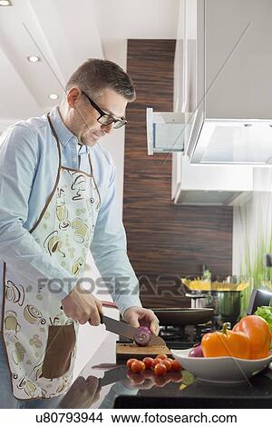 Picture - Mid-adult man cutting vegetables at kitchen counter. Fotosearch