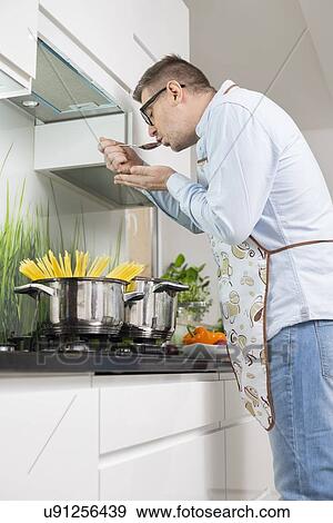 Mid-adult man tasting food while cooking in kitchen View Large Photo Image Stock Photo - Mid-adult man tasting food while cooking in kitchen. Fotosearch