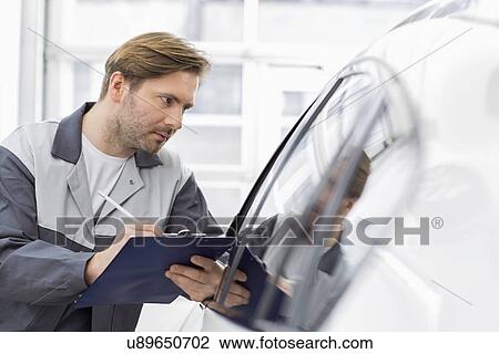 Mid adult repair worker writing on clipboard while examining car in workshop View Large Photo Image Stock Image - Mid adult repair worker writing on clipboard while examining car in workshop. Fotosearch