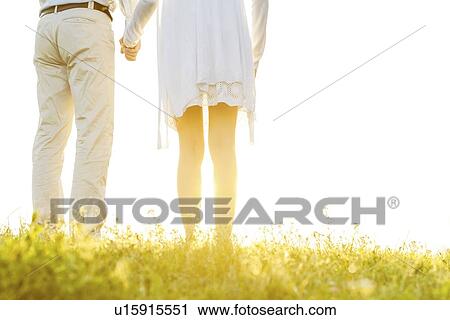 Midsection back view of couple holding hands on grass against sky View Large Photo Image Stock Image - Midsection back view of couple holding hands on grass against sky. Fotosearch