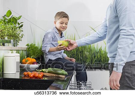 Stock Photograph - Midsection of father giving pear to son in kitchen. Fotosearch