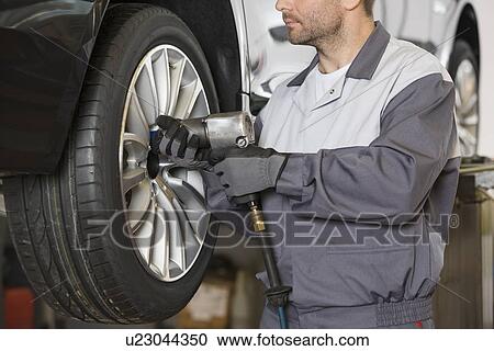 Stock Image - Midsection of male mechanic repairing car's wheel in workshop. Fotosearch