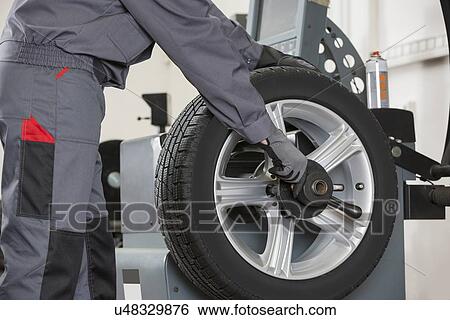 Stock Photograph - Midsection of male mechanic repairing car's wheel in repair shop. Fotosearch