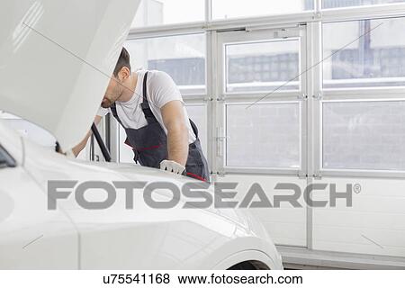 Stock Photo - Midsection of male technician repairing car engine in workshop. Fotosearch