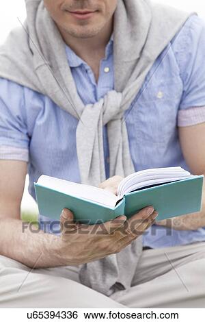 Stock Photograph - Midsection of man holding book in park. Fotosearch