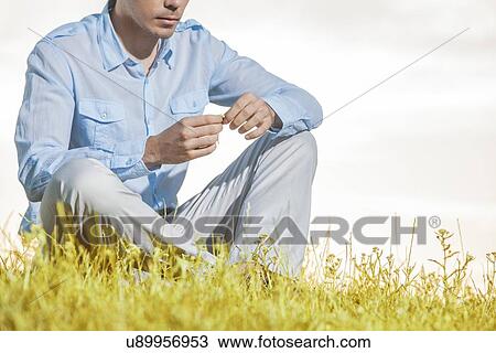 Midsection of man holding flower while sitting on grass against clear sky View Large Photo Image Stock Image - Midsection of man holding flower while sitting on grass against clear sky. Fotosearch