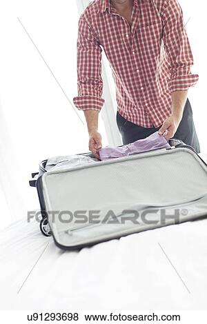 Midsection of young businessman packing luggage in hotel room View Large Photo Image Stock Photo - Midsection of young businessman packing luggage in hotel room. Fotosearch