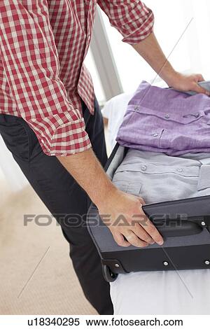 Stock Photography - Midsection of young man unpacking suitcase in hotel room. Fotosearch