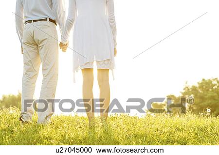 Midsection rear view of couple holding hands on grass against sky View Large Photo Image Stock Image - Midsection rear view of couple holding hands on grass against sky. Fotosearch