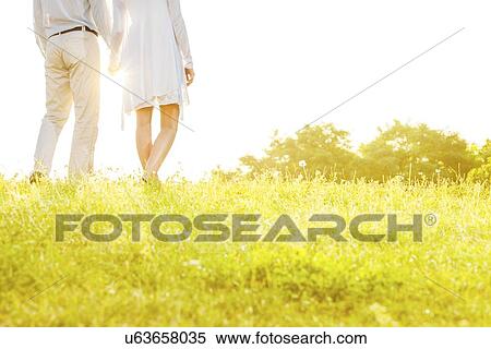 Midsection rear view of couple holding hands while standing on grass against sky View Large Photo Image Stock Photography - Midsection rear view of couple holding hands while standing on grass against sky. Fotosearch