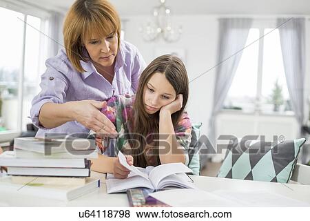 Stock Photo - Mother assisting bored girl in studying at home. Fotosearch