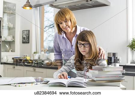Mother assisting daughter in doing homework in kitchen View Large Photo Image Picture - Mother assisting daughter in doing homework in kitchen. Fotosearch