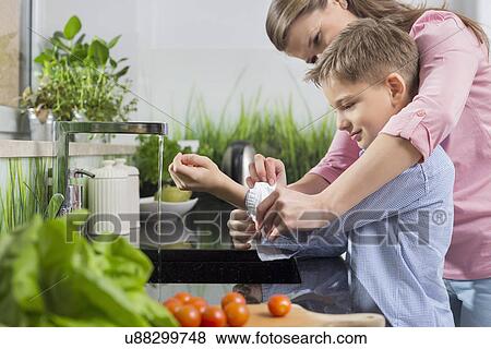 Mother assisting son in folding sleeves while washing hands in kitchen View Large Photo Image Stock Photo - Mother assisting son in folding sleeves while washing hands in kitchen. Fotosearch