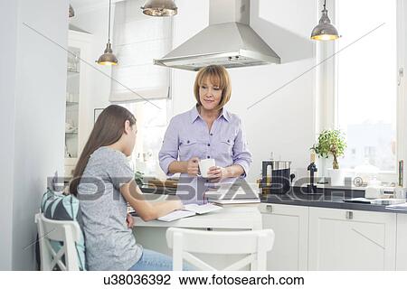 Mother holding coffee cup while looking at daughter studying in kitchen View Large Photo Image Stock Image - Mother holding coffee cup while looking at daughter studying in kitchen. Fotosearch