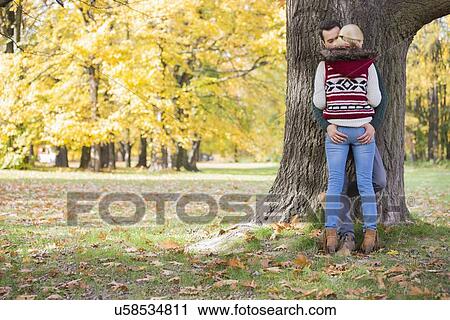 Stock Image - Passionate couple against tree trunk in park during autumn. Fotosearch