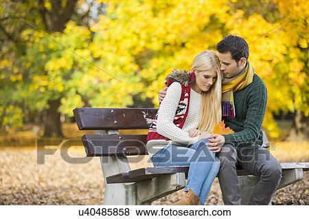 Passionate young man hugging shy woman on park bench during autumn View Large Photo Image Stock Photo - Passionate young man hugging shy woman on park bench during autumn. Fotosearch