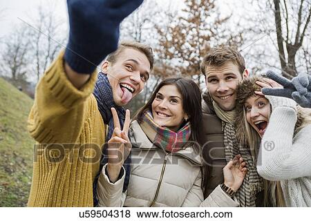 Stock Photo - Playful couples gesturing while taking self portrait in park. Fotosearch