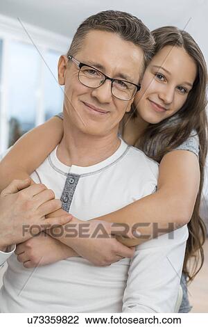 Stock Image - Portrait of affectionate girl embracing father from behind at home. Fotosearch