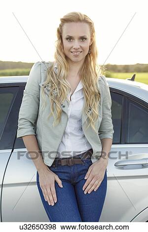 Portrait of attractive young woman standing by car at countryside View Large Photo Image Stock Photo - Portrait of attractive young woman standing by car at countryside. Fotosearch