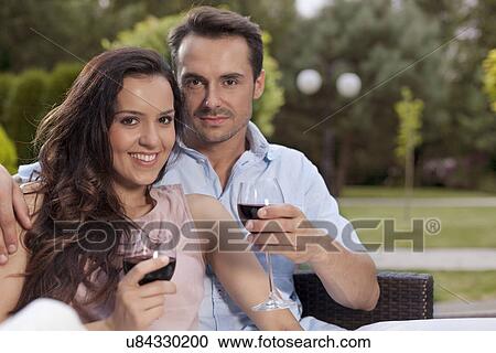 Stock Image - Portrait of beautiful young couple having red wine in park. Fotosearch