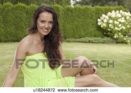 Stock Image - Portrait of beautiful young woman in sundress relaxing in park. Fotosearch