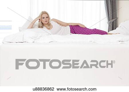 Portrait of beautiful young woman lying in bed at hotel room View Large Photo Image Stock Image - Portrait of beautiful young woman lying in bed at hotel room. Fotosearch