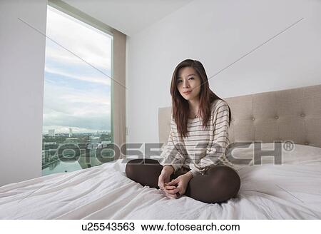 Portrait of beautiful young woman sitting on bed View Large Photo Image Stock Image - Portrait of beautiful young woman sitting on bed. Fotosearch