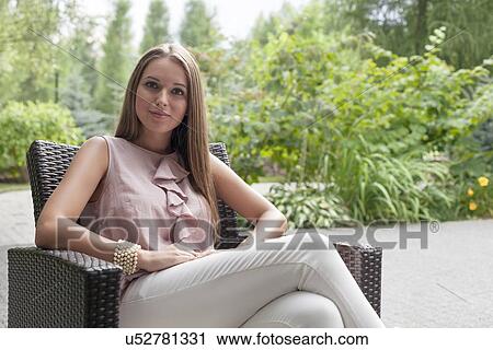 Stock Image - Portrait of beautiful young woman sitting on chair in summer park. Fotosearch