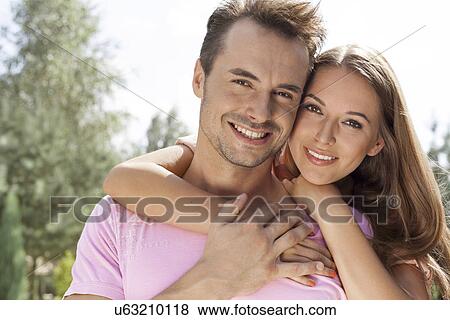 Stock Photo - Portrait of beautiful young woman embracing man in park. Fotosearch